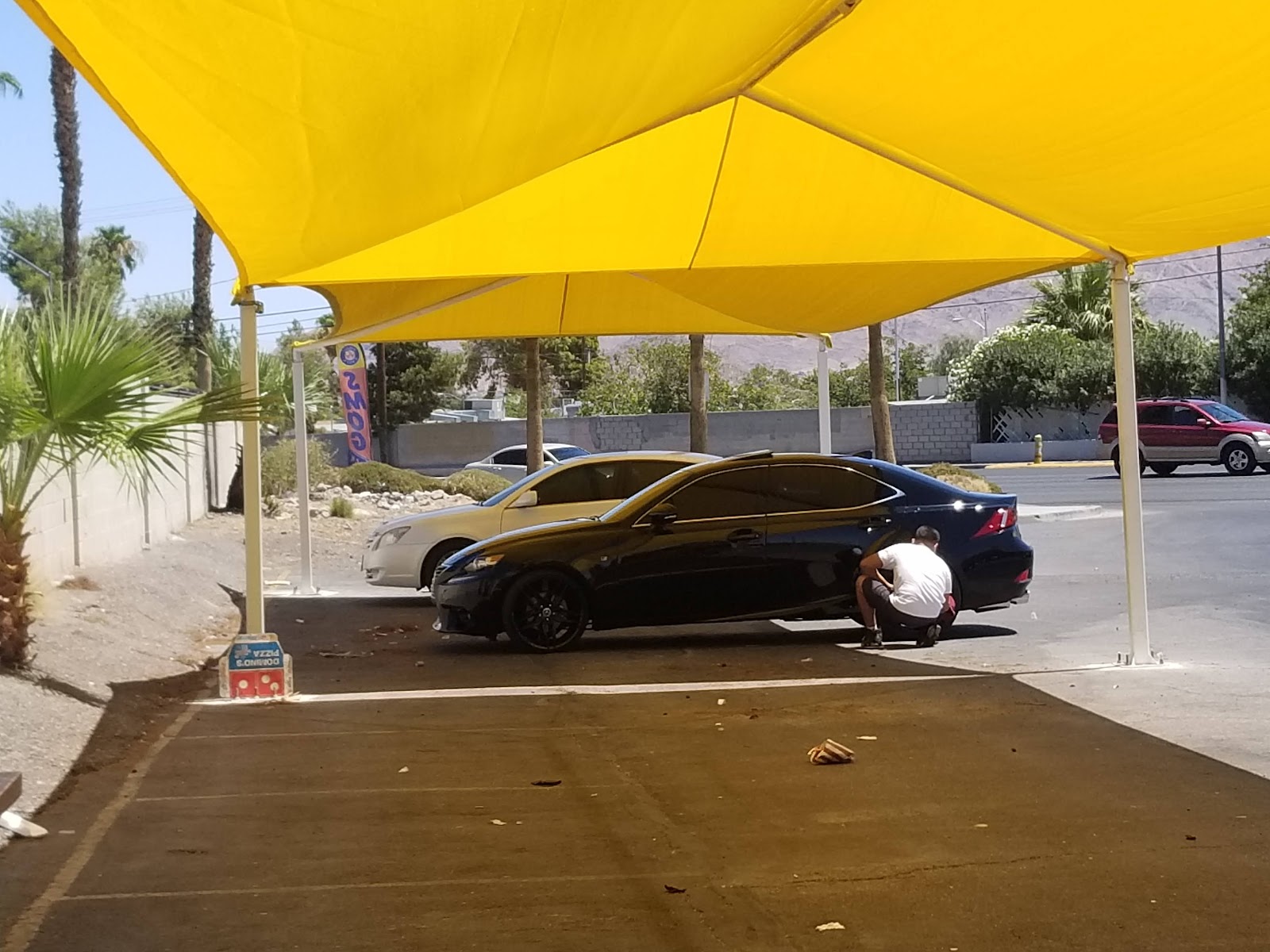 Worker hand-drying a black Lexus under a yellow shade canopy