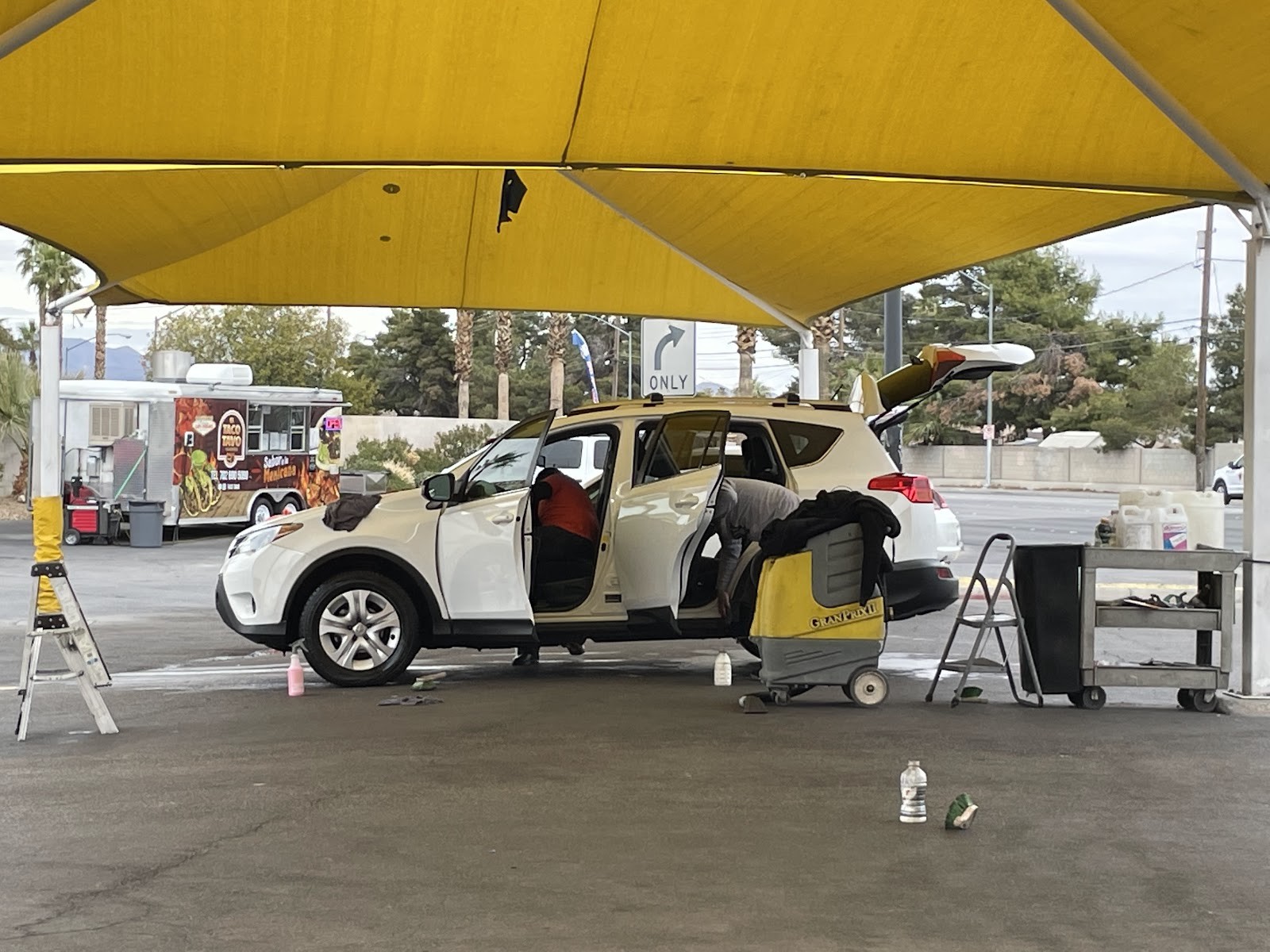 Two workers detailing a white SUV with an extractor under the shade canopy